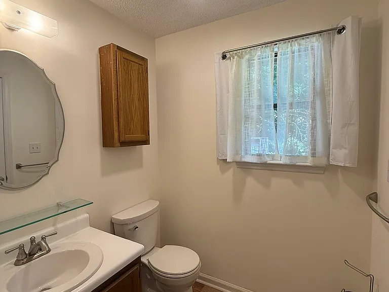 En-suite bath has shower, with large shower head/sprayer, grab bar, hotel curtain, vent fan, chair-height toilet, and window that can be opened or covered with blackout curtain.