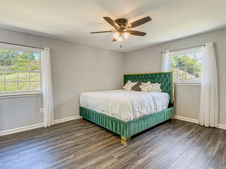 Spacious bedroom with two large windows, ceiling fan, and durable wood-look flooringideal for restful nights.