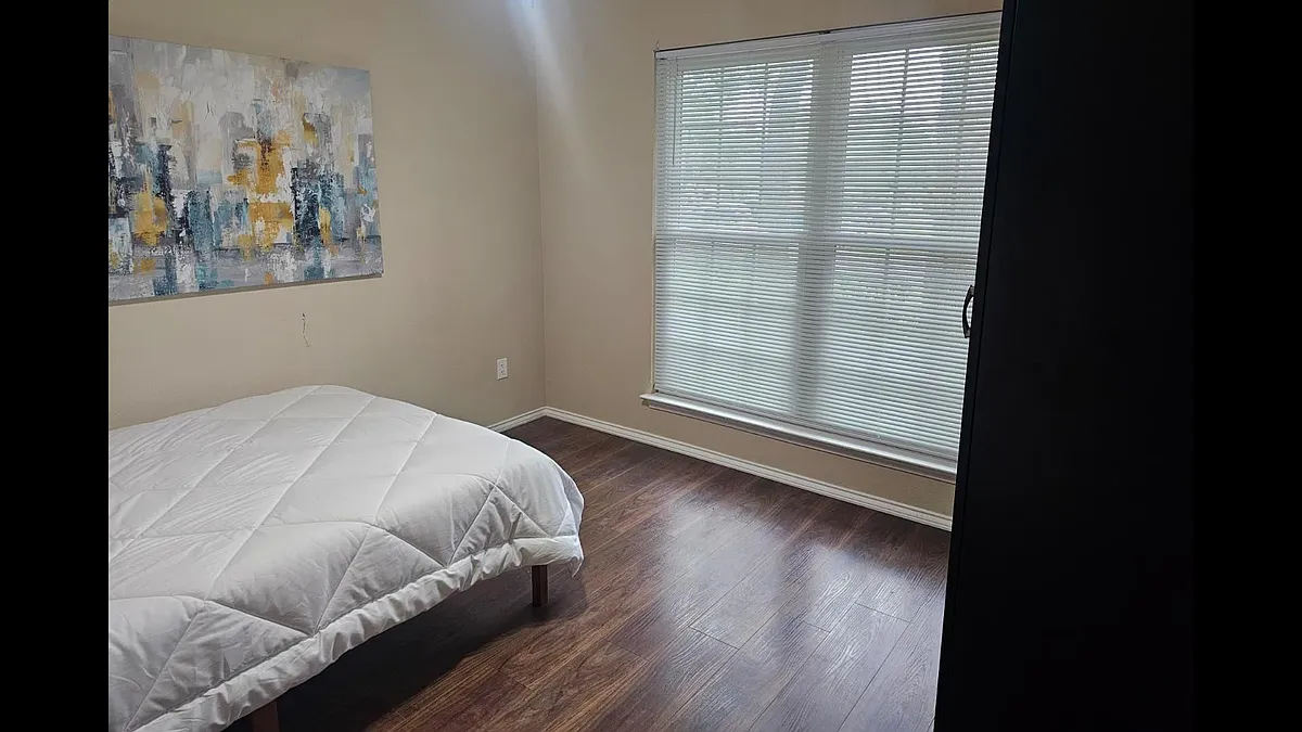 Private bedroom with wood-style flooring, a large window with blinds, and ample wall space for storage or a desk. - Sabinal Trl