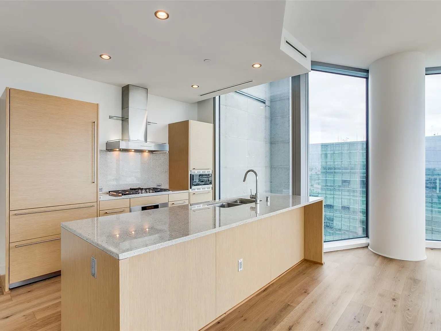Gourmet kitchen featuring a large island with sink, stainless steel appliances, wood-finish cabinetry, and recessed lighting