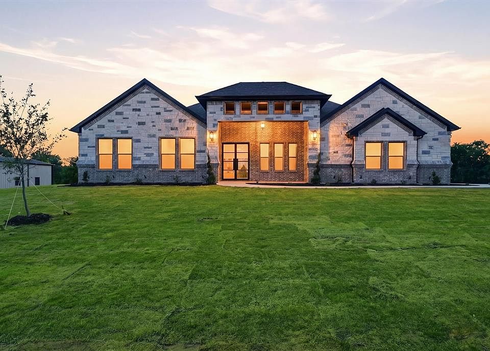 Back of house at dusk with a yard, brick siding, and stone siding