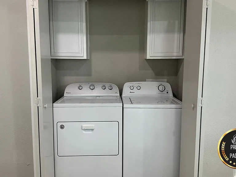 Convenient in-home laundry closet with washer and dryer plus upper cabinets for storing detergents and supplies.
