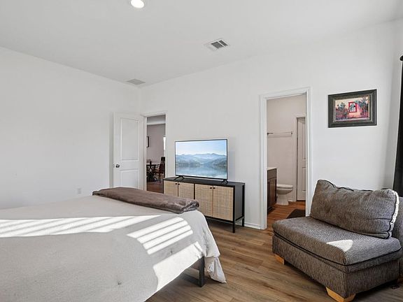 Spacious bedroom with a seating area, TV console, and convenient en-suite bathroom access, plus easy-care flooring.