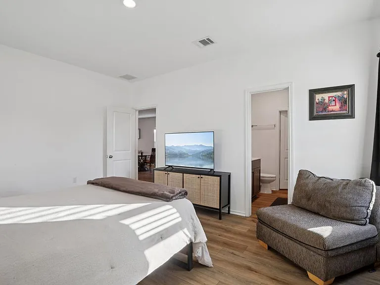 Spacious bedroom with a seating area, TV console, and convenient en-suite bathroom access, plus easy-care flooring.