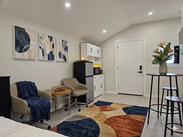Furnished bedroom suite with seating area, mini fridge and microwave, plus a bistro table and secure entry door.