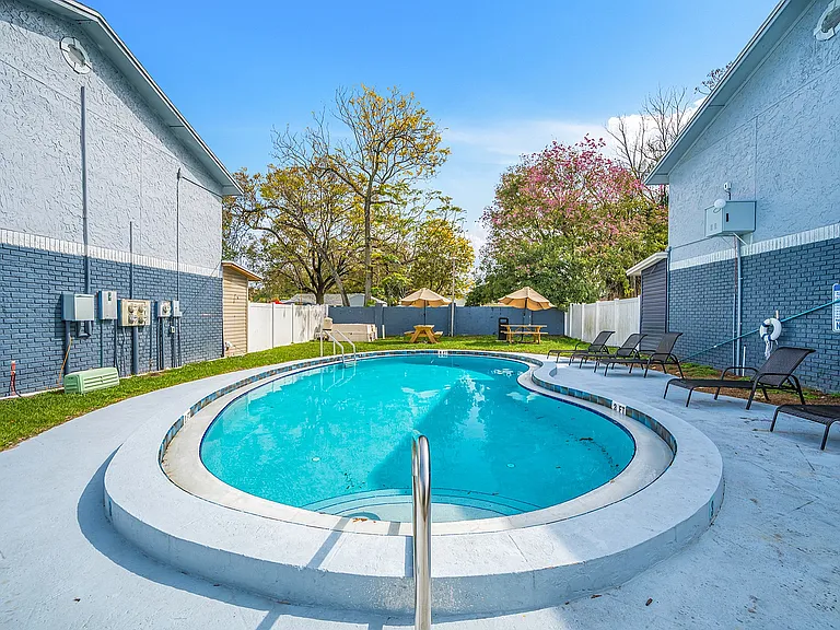 Inviting outdoor pool area with lounge chairs, surrounded by lush greenery and patio umbrellas, perfect for relaxation and enjoyment.