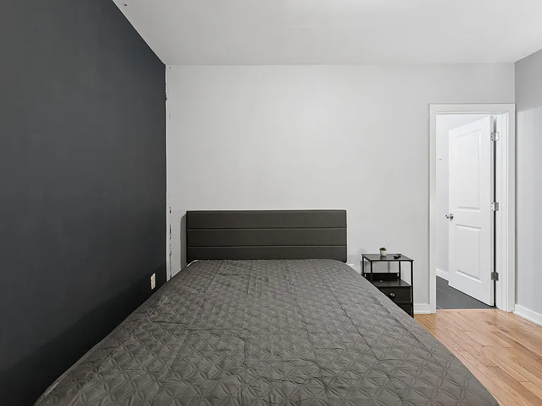 Furnished bedroom with a full-size bed, nightstand, and hardwood floors, plus a bold accent wall for added style.