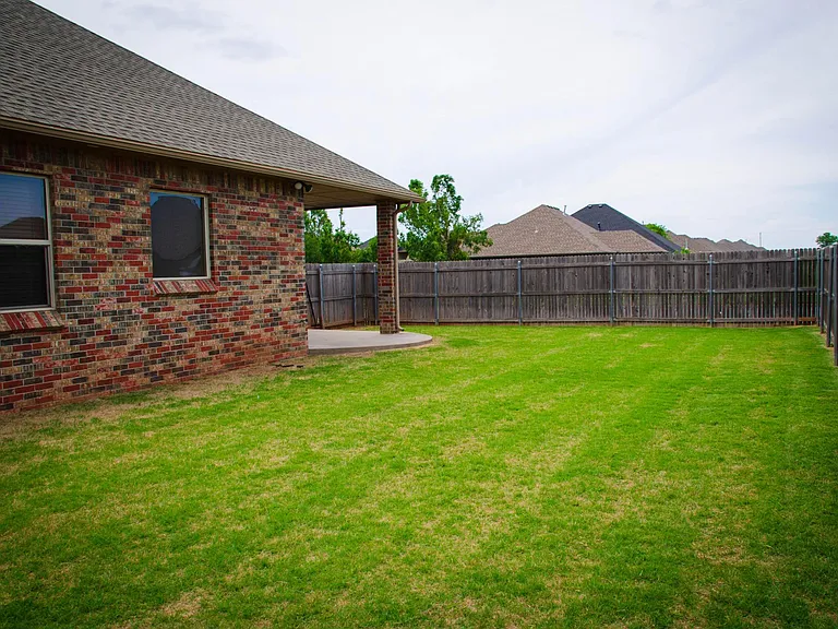 Backyard has a wooden fence protecting the property. Large grassy backyard.
