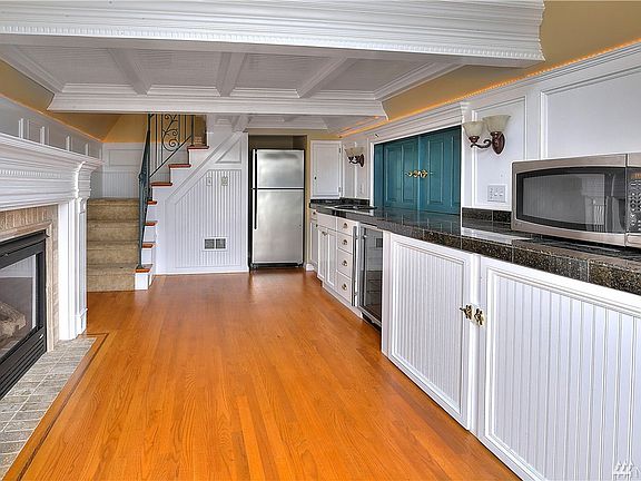 Boat house kitchenette features extensive mill work, accent lighting, refrigerator, small beverage fridge, tile counters, gas fireplace with tile surround and hardwood floors.