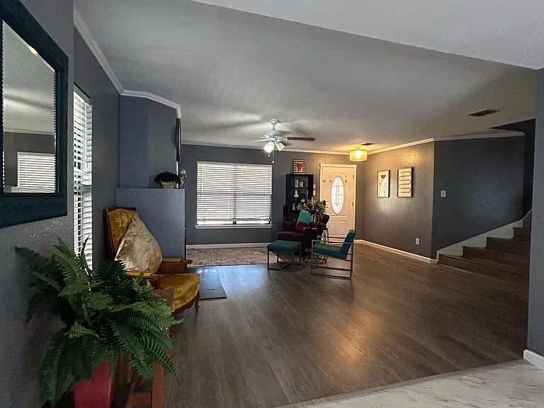 Open living area with wood-style floors, ceiling fan, and large window; foyer entry and staircase provide easy flow.