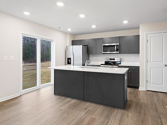 Island kitchen with gray cabinets and glass sliding door in a DRB Homes Glenshaw plan at The Village