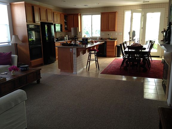 Great room, kitchen and dining area. Large center island with faux granite counters. Gas fireplace with fake logs is to the right. French door is at covered patio. The kitchen flooring is linoleum. Carpet was newly installed in March 2016.