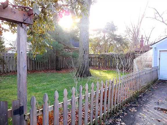 Fenced in back yard with small greenhouse attached to small, 1-car garage.