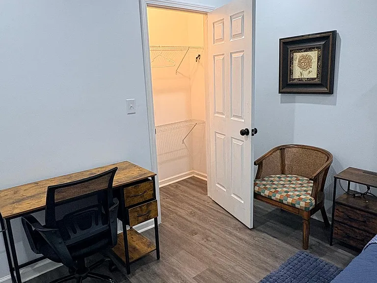 Furnished bedroom featuring a work desk and chair, accent seating, and a walk-in closet with shelving for easy storage.