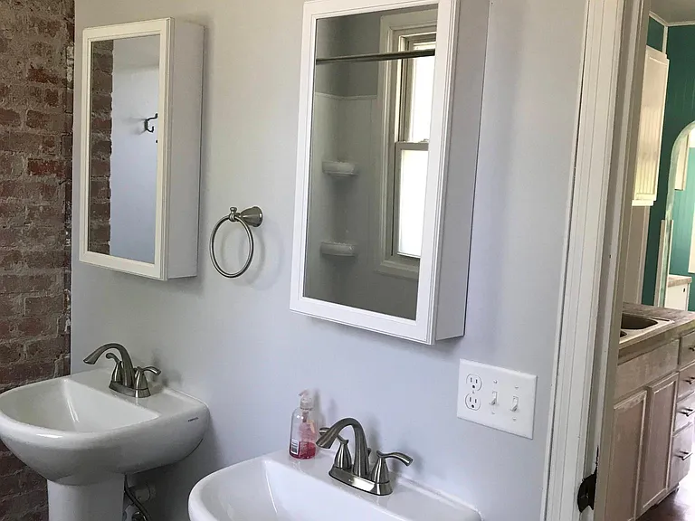 Bathroom with new sinks, lightings, medicine cabinets & exposed brick.
