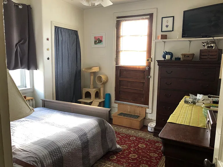 Photo from 2021. Back room, being used as a bedroom. Door is to the deck. Behind the grey curtain is a shallow closet, great for shoes or sweaters