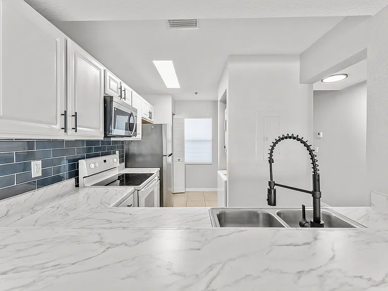 Modern kitchen with sleek marble countertops, stylish black hardware, and contemporary stainless steel appliances.