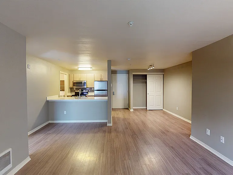 Apartment kitchen with stainless steel appliances, dining and living room with wood-style flooring.