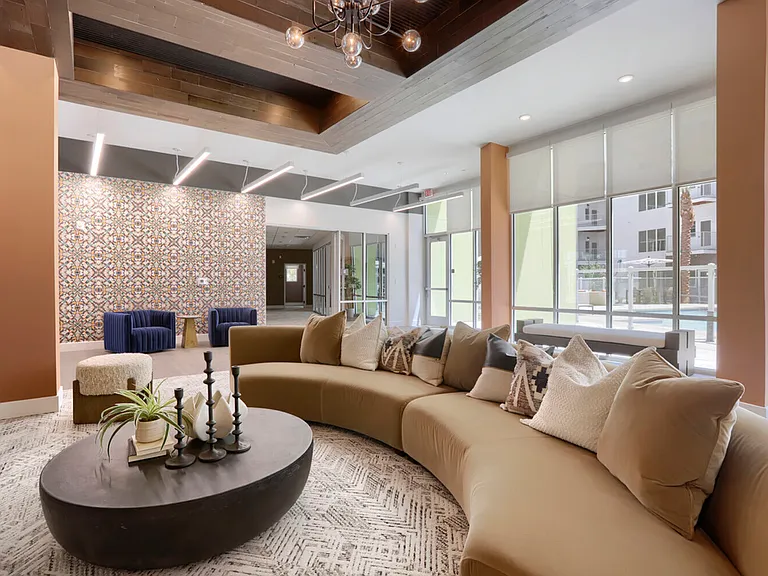 Kick back in style. The main lounge anchors the Garrett Uptown clubhouse with a statement curved sectional, bold accent tile, and natural light pouring in from the pool courtyard.
