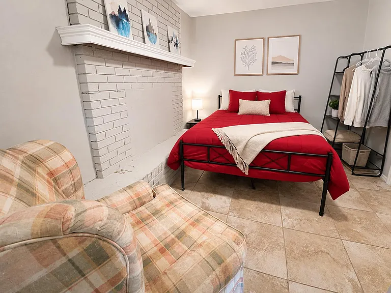 Furnished bedroom with a comfortable bed, bedside table with lamp, and open garment rack for easy everyday storage.