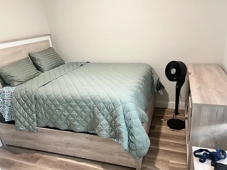 Furnished bedroom with a full-size bed, matching dresser, and open floor space for easy movement and storage.