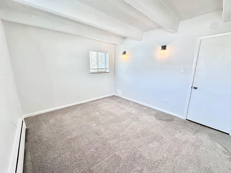 Bright and inviting empty room with plush carpet, white walls, and natural light from a small window. Elegant wall sconces add a modern touch. Bright and inviting empty room with plush carpet, white walls, and natural light from a small window. Elegant wa