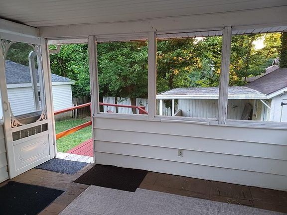 Screened in porch with view of carport and small garage in the background.