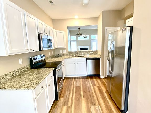 Bright, elegant kitchen with granite countertops, stainless steel appliances, white cabinetry, and wood flooring. Open layout with view into living area.