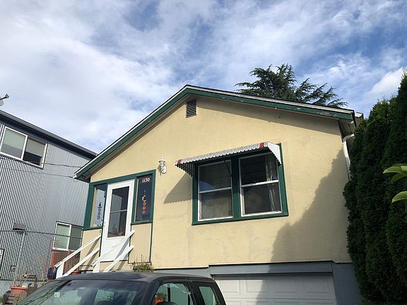 front of house shows the driveway with one car garage on lower level. there is also a workbench in the garage.