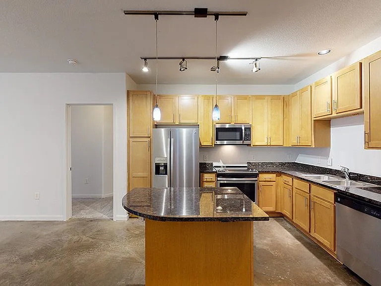 Apartment kitchen with stainless steel appliances, granite countertops and wood-style flooring.