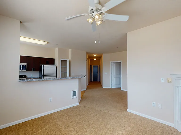 Apartment kitchen with stainless steel appliances, dining and living room with plush carpet flooring.