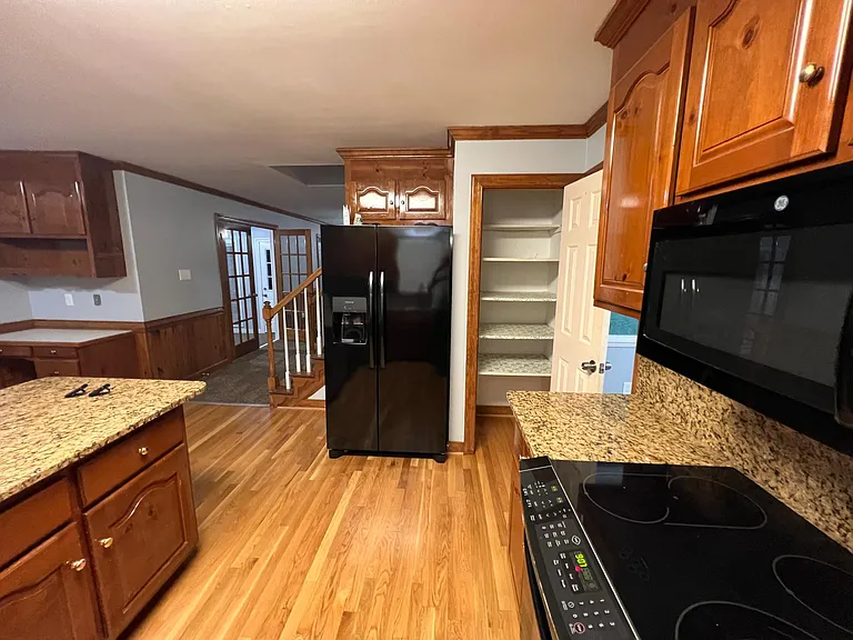 Photo of kitchen, entryway to the dining room pictured to the right, pantry straight ahead. New fridge, to the left of the fridge is the stairs to the upstairs and also open area to the florida room and living room.