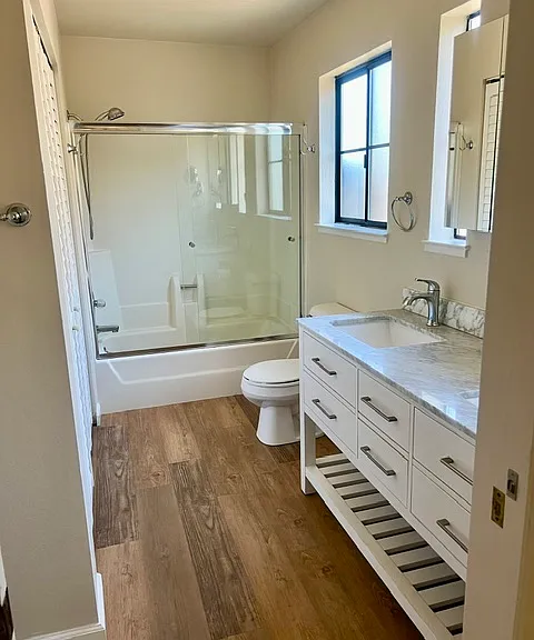 bathroom with carrera marble counter top, shower and shower door, laundry area located behind folding doors.