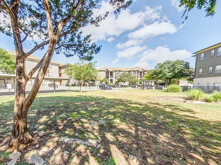 Fenced in dog park with large green space and shade trees