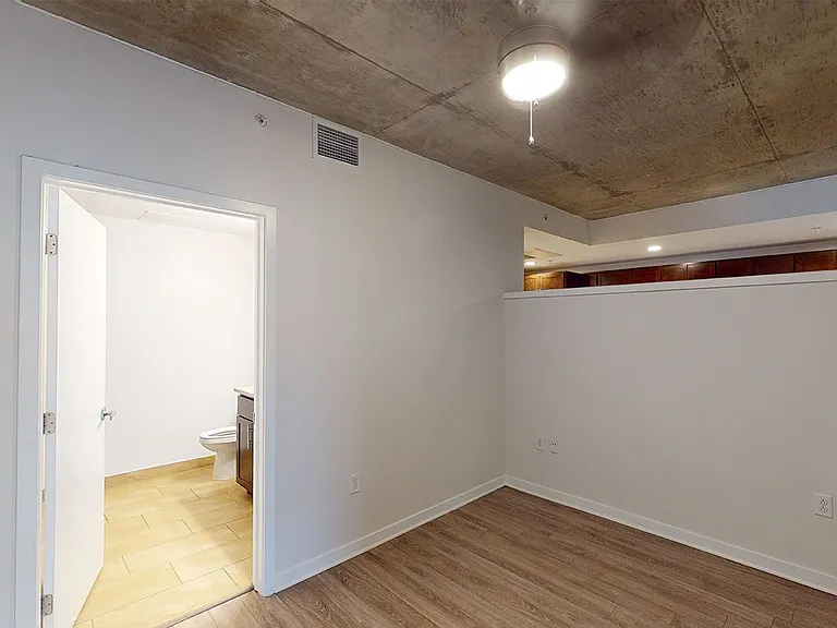 Spacious apartment bedroom with attached bathroom and wood-style flooring.