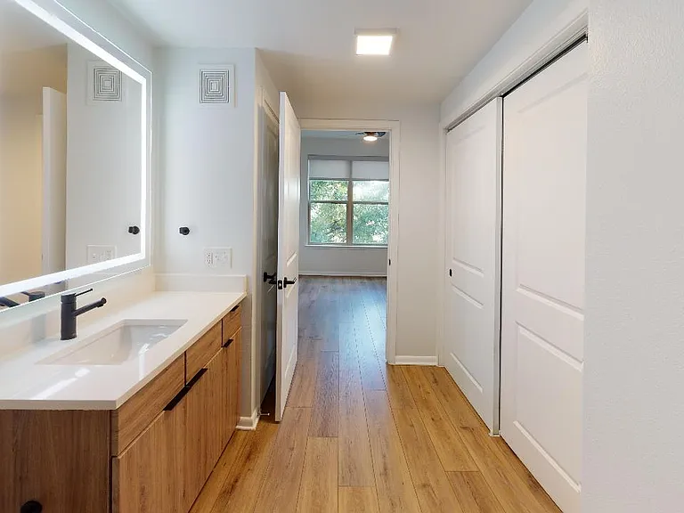 Apartment bathroom with wood-style flooring and LED vanity mirror.