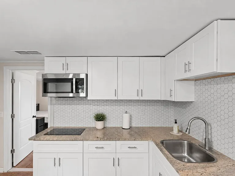 Clean U-shaped kitchen with white shaker cabinets, hex-tile backsplash, granite-look counters, and stainless sink/microwave.