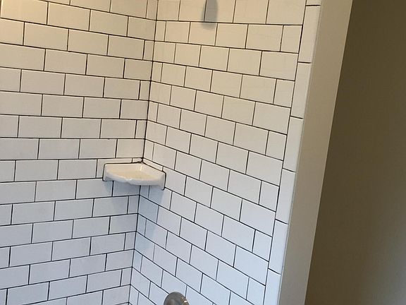 Upstairs shower has subway smaller subway tiles with dark gr