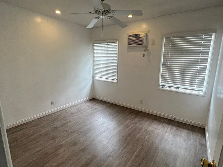 Large secondary bedroom with ceiling fan, wall ac unit, window blinds and closet.