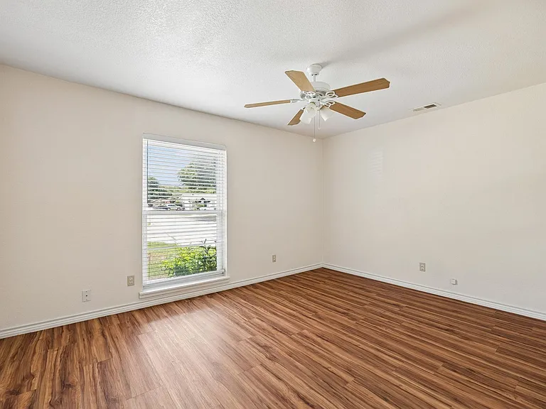 Spacious room featuring wood-finish flooring, a ceiling fan with light fixture, and a window with horizontal blinds