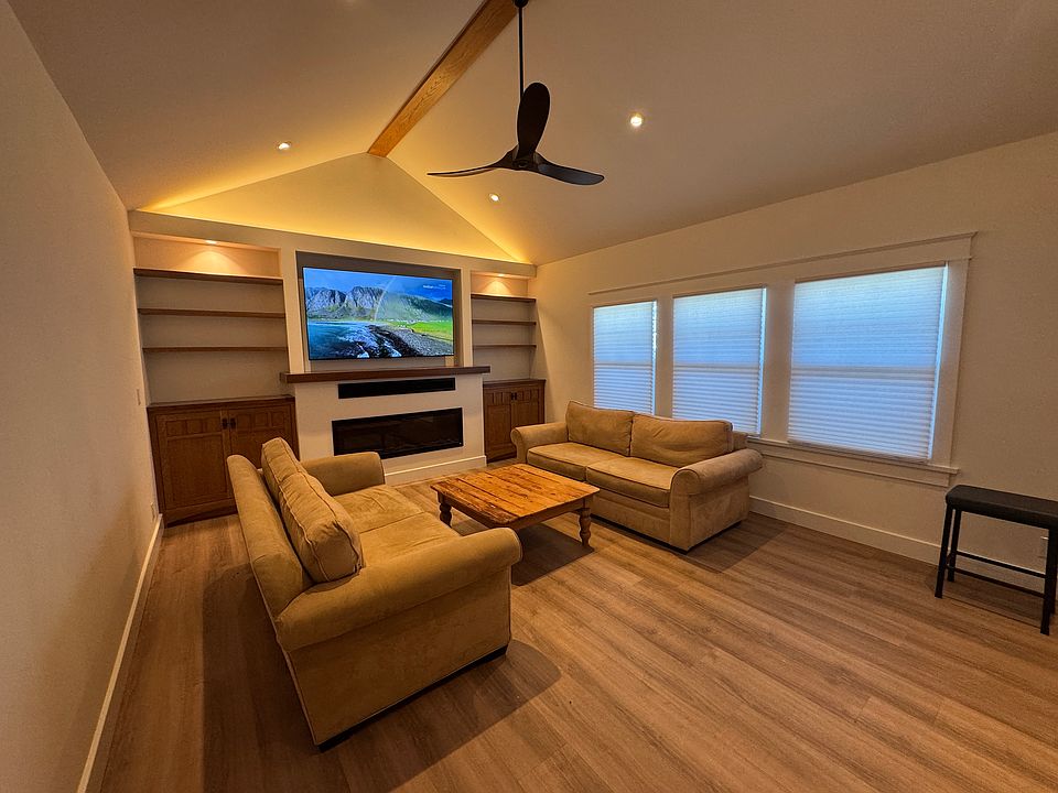 View of living area from front door with over 12 foot ceilings and a fan. Walnut mantle and top of side cabinets with customer oak cabinets and oak shelving.