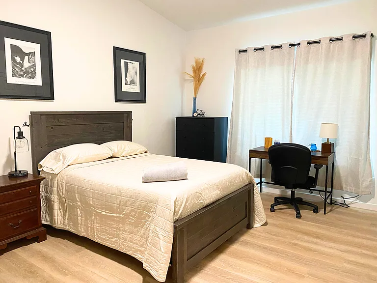 Cozy bedroom featuring a comfortable bed, dresser, nightstand, and quality lighting. A dedicated workstation with desk and chair is perfect for productivity. Enjoy privacy with room-darkening blinds and curtains. Ideal for a restful and functional living