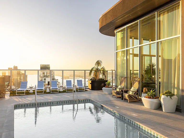 Luxurious rooftop pool with breathtaking city and waterfront views, stylish loungers, and elegant glass-paneled architecture.