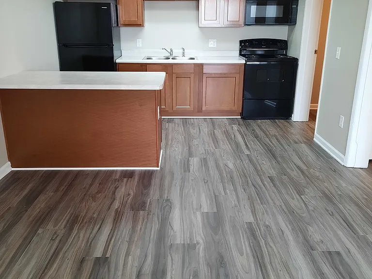 Kitchen in the one bedroom floorplan showing an open concept with light brown cabinets, black appliances and light gray countertops