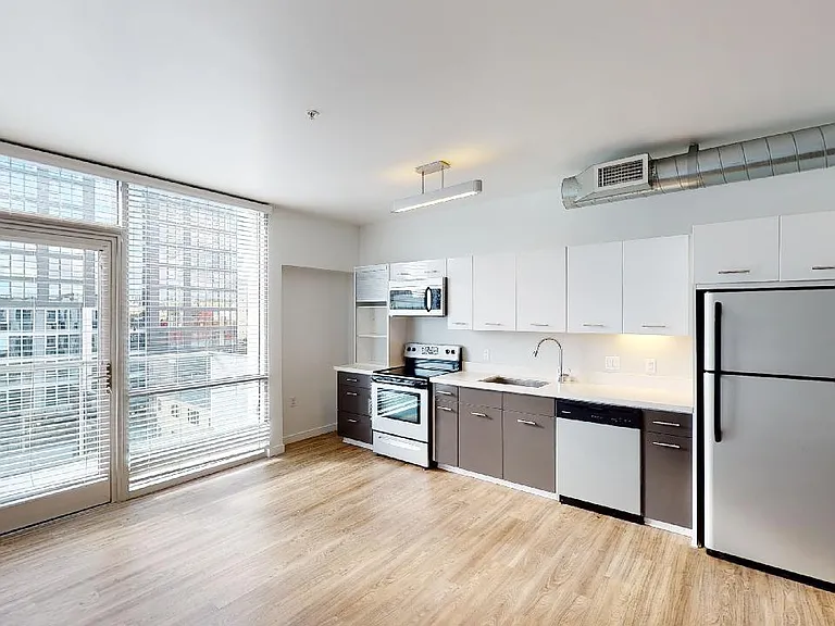 Apartment kitchen with stainless steel appliances, dining and living room with wood-style flooring.