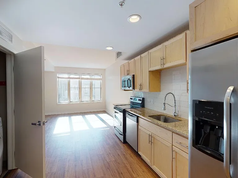 Apartment kitchen with stainless steel appliances, granite countertops and wood-style flooring.