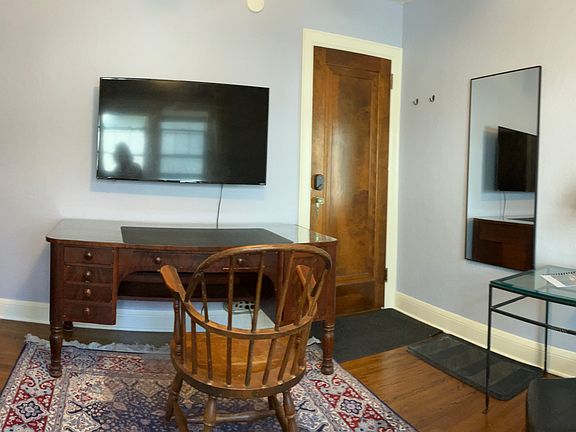 There is a beautiful, large desk with 50" TV mounted above, a classy glass side table with coffee and lamp and Poang IKEA comfy chair.