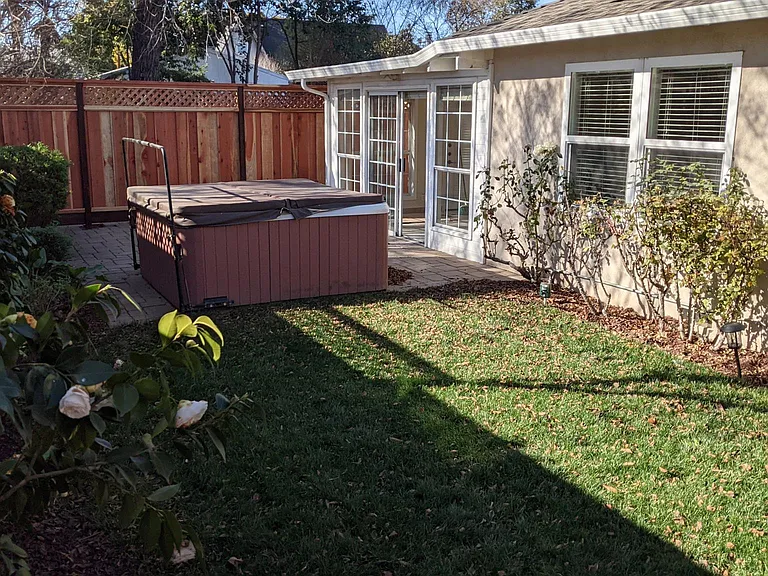 View of yard with lawn, patio, spa. 
(Cottage is located behind the tall fence)