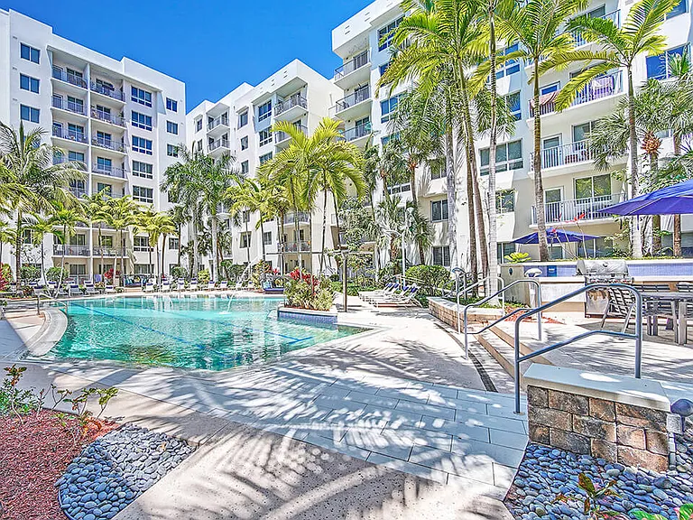 Luxury apartment resort-style pool with palm trees, sun loungers, and landscaped courtyard