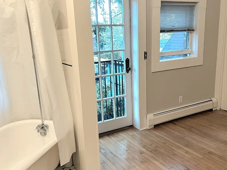 A serene retreat featuring a classic tub, sunlit Juliet balcony, and charming dressing space.
